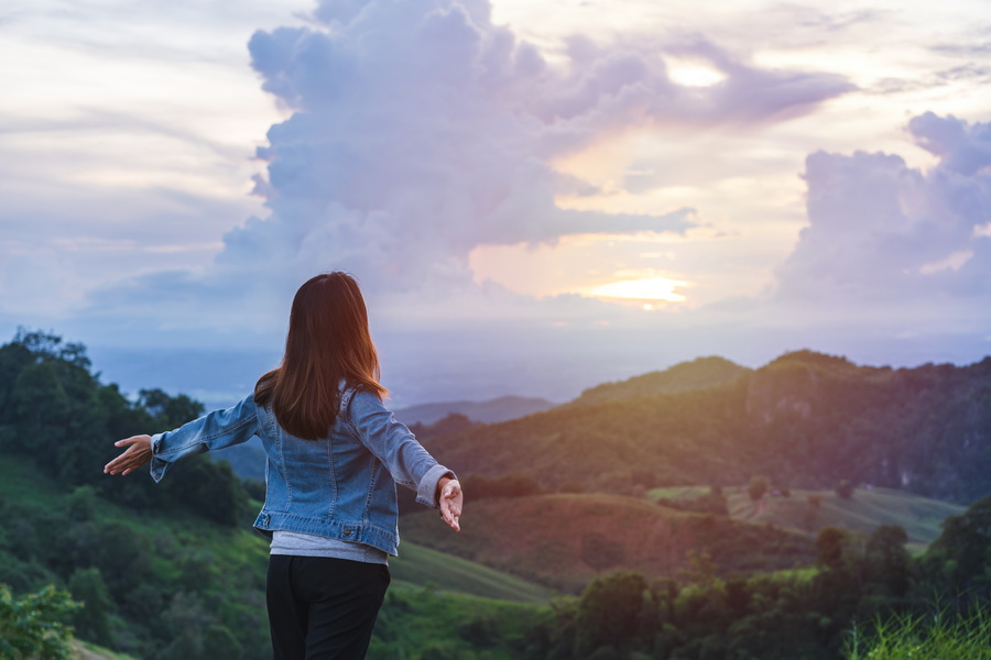 Happy young woman traveler relaxing and looking at the beautiful sunset on the top of mountain